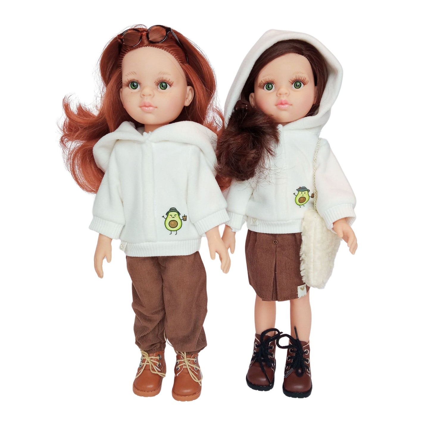 Two Paola Reina dolls wearing white hoodies with an avocado print, paired with brown corduroy pants and a skirt, styled with boots and accessories.