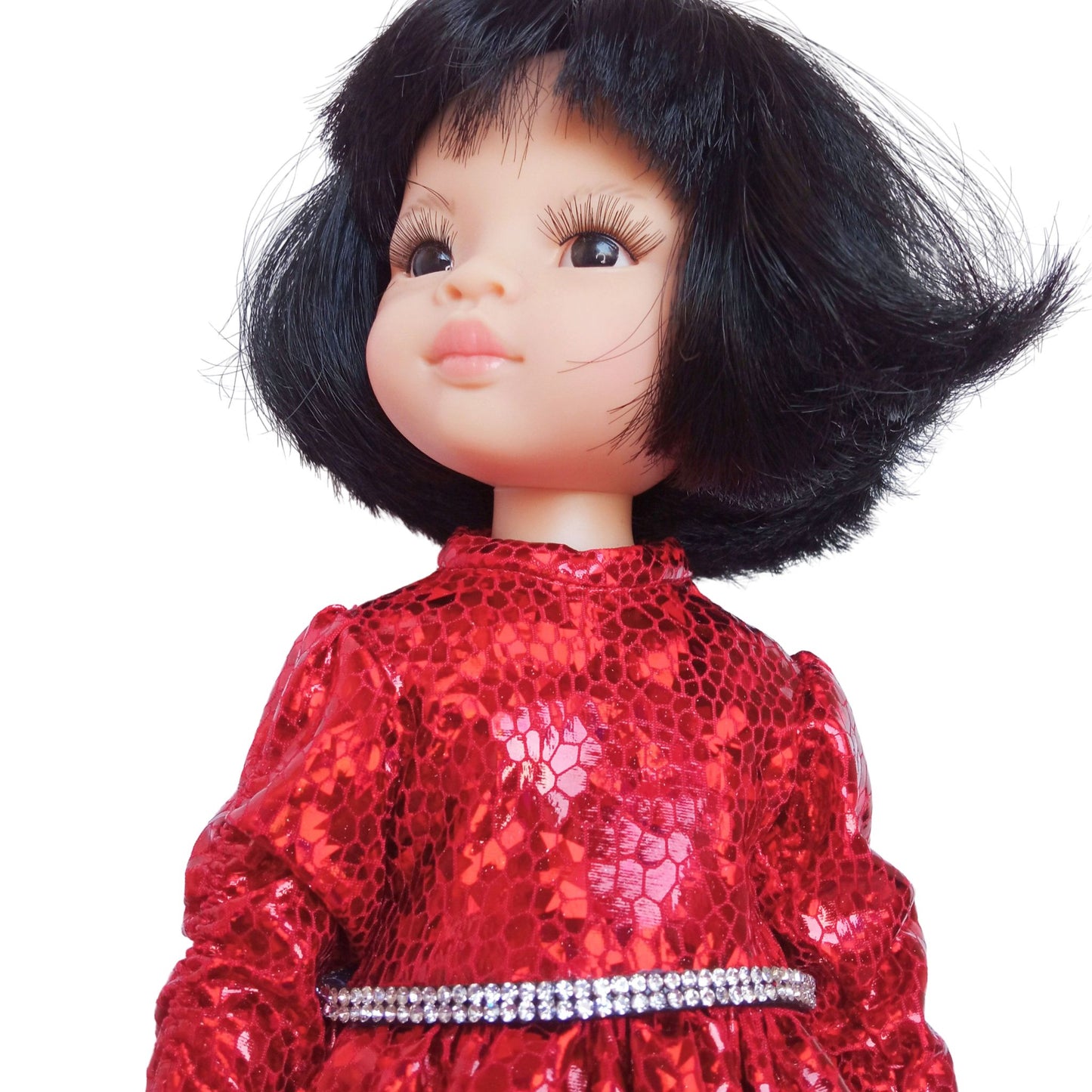 Paola Reina 32 cm doll wearing a red sparkling dress with a rhinestone belt and black patent leather shoes, standing against a white background.