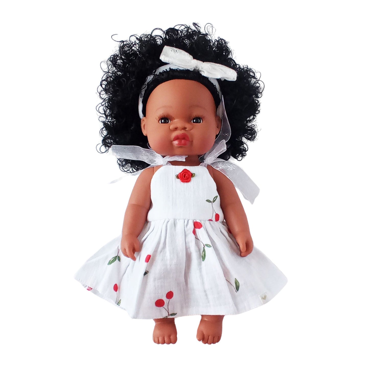 Dark-skinned curly-haired doll wearing a white summer cotton sundress with cherry print and red rose detail, designed for 34 cm dolls like Paola Reina or Baby Born.