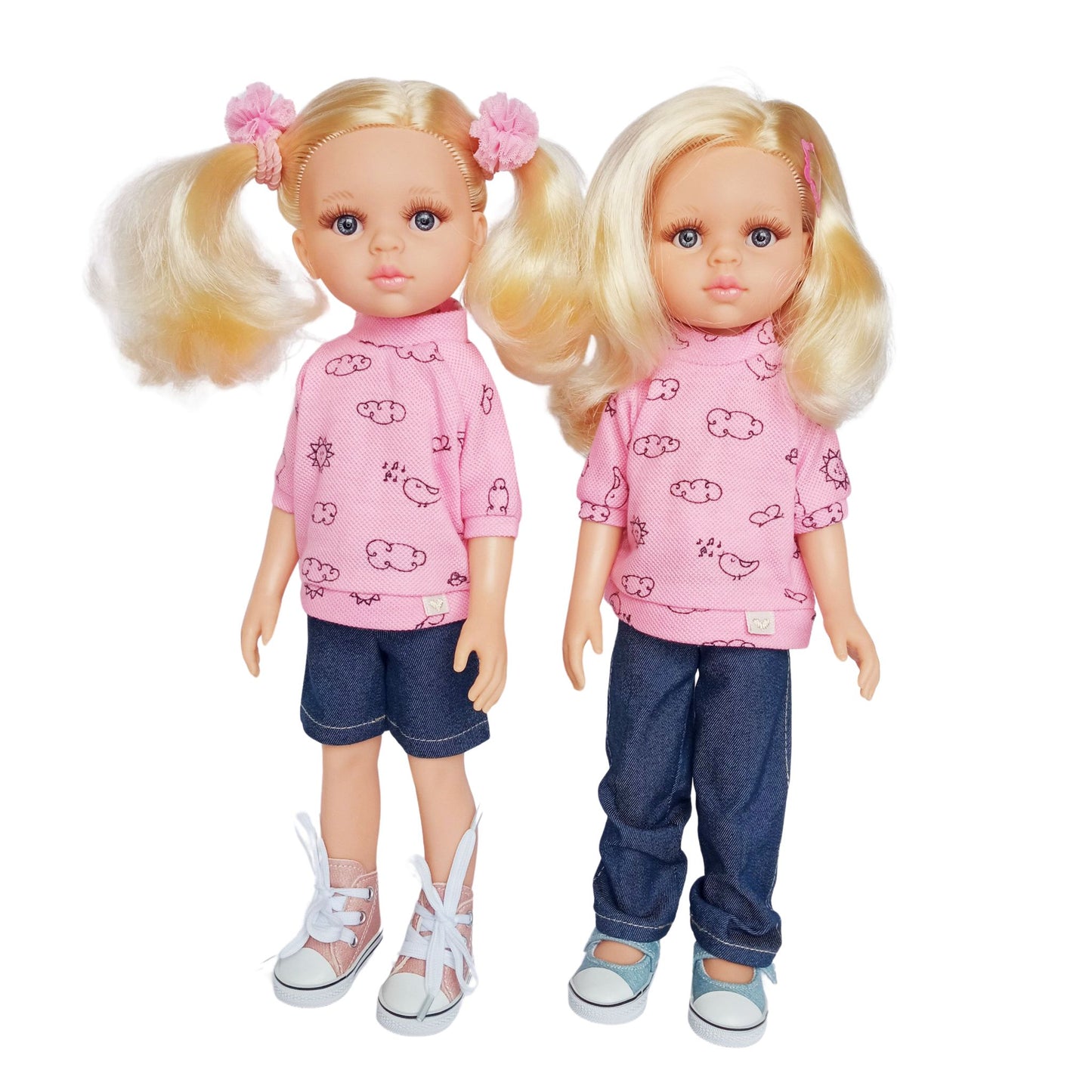 Two Paola Reina 32 cm dolls wearing pink blouses with cloud prints, one styled with denim pants and the other with denim shorts and sneakers.