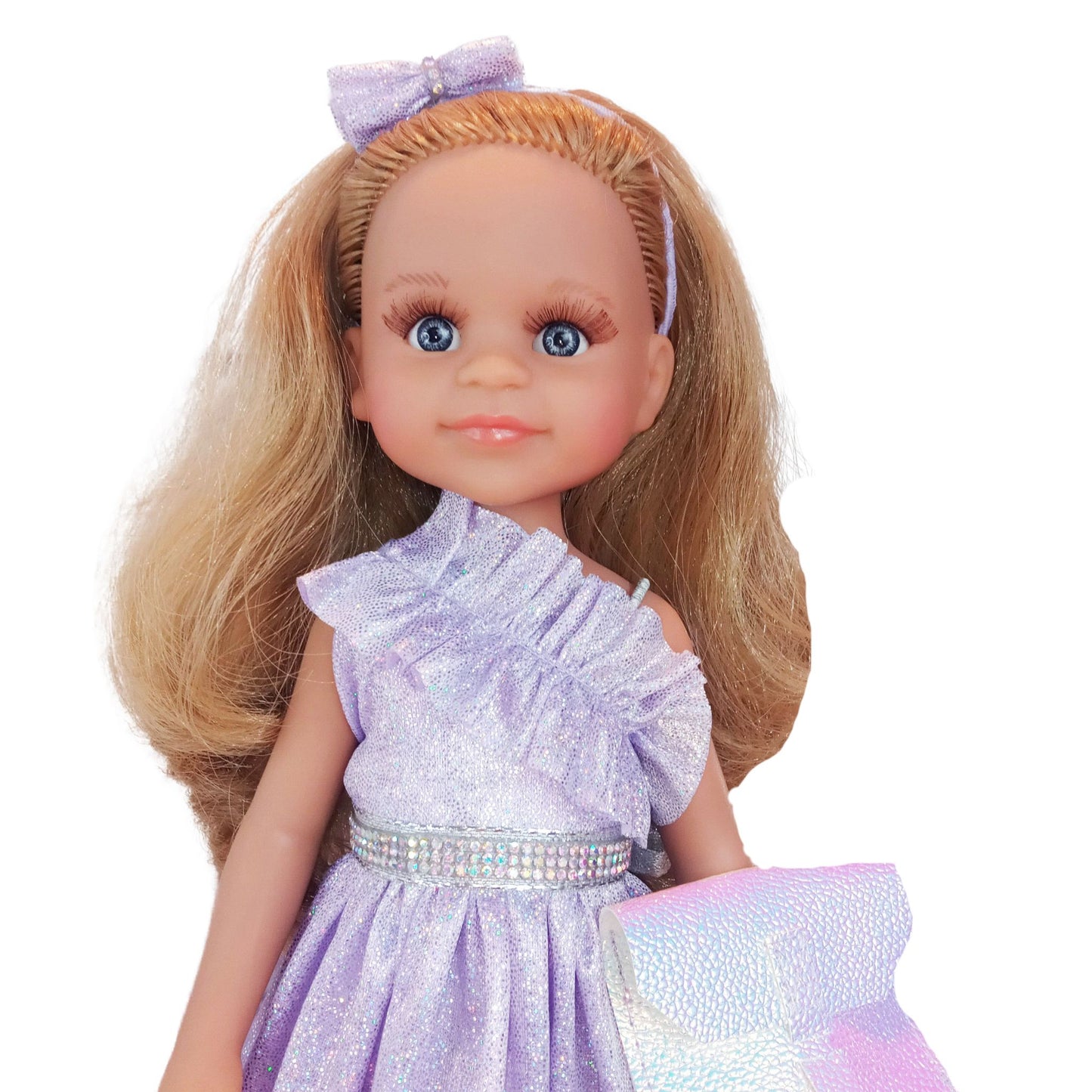 Paola Reina 32 cm doll wearing a lilac dress with ruffles, matching headband, holographic clutch, and glitter sneakers.