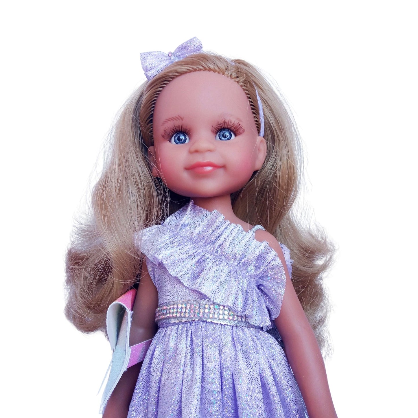 Paola Reina 32 cm doll wearing a lilac dress with ruffles, matching headband, holographic clutch.