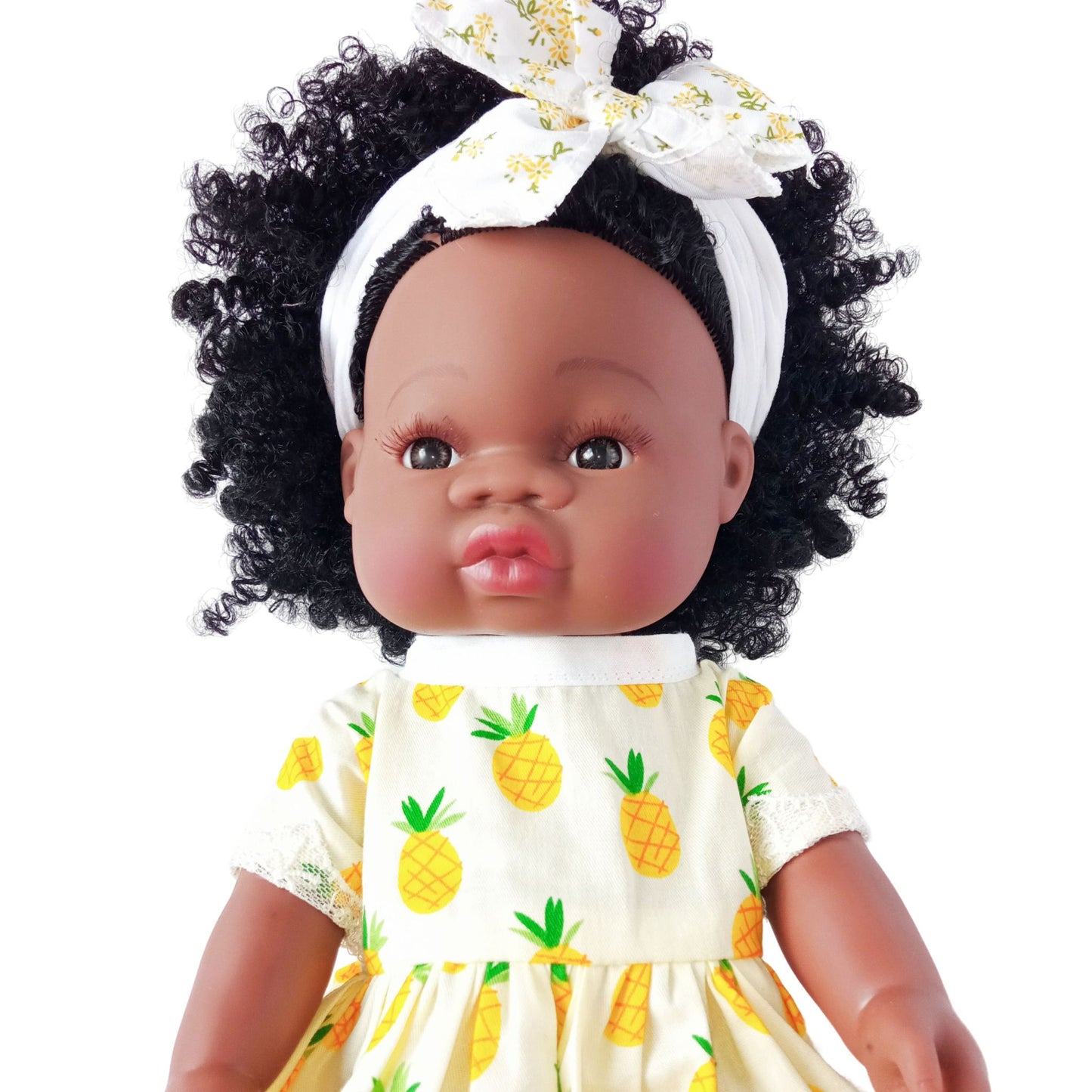 Doll wearing a yellow summer dress with pineapple print and lace hem, paired with a matching headband with bow, suitable for 34 cm dolls like Paola Reina or Baby Born