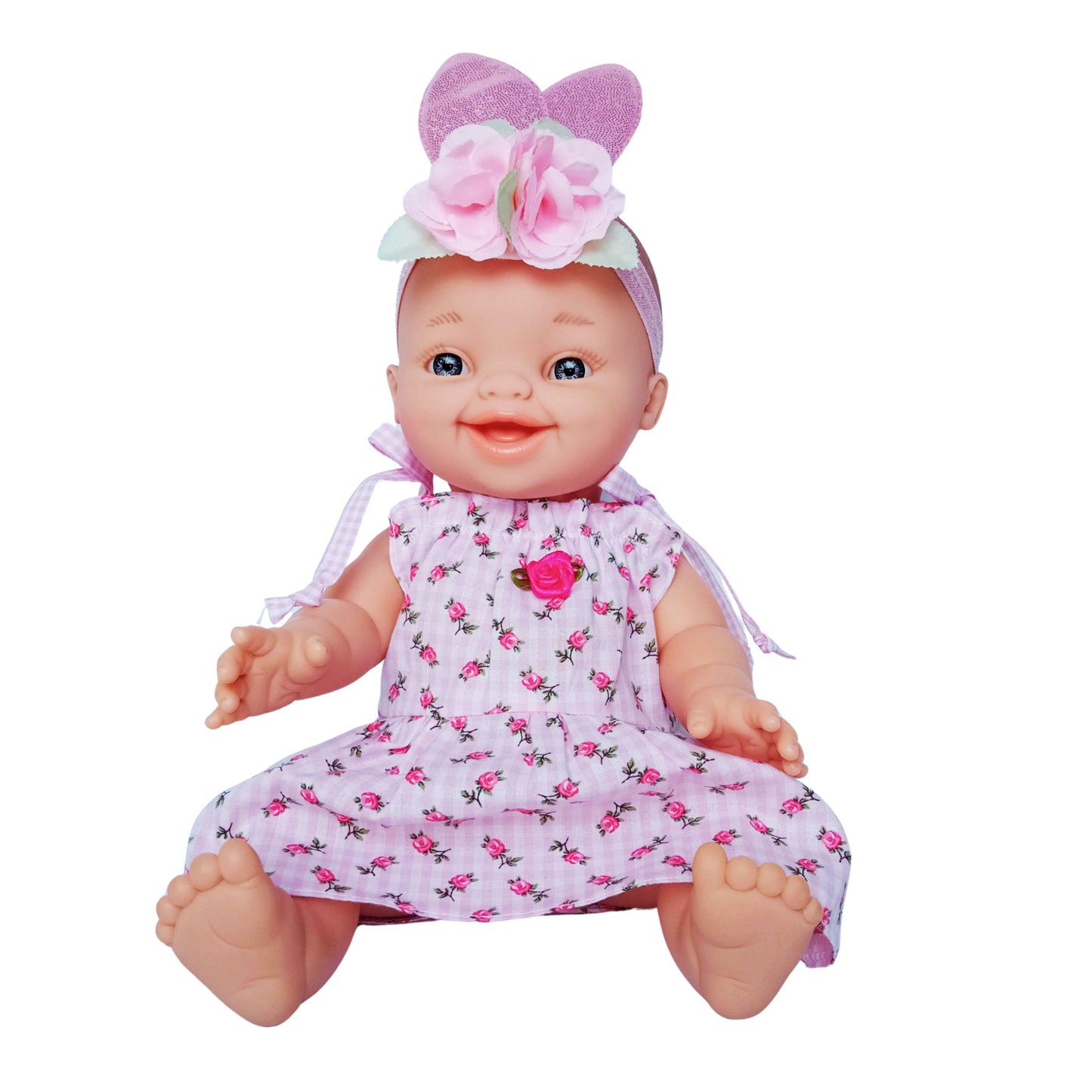 Smiling baby doll wearing a pink floral cotton summer dress with shoulder ties and rosebud decoration, made for 34 cm dolls like Paola Reina or Baby Born.