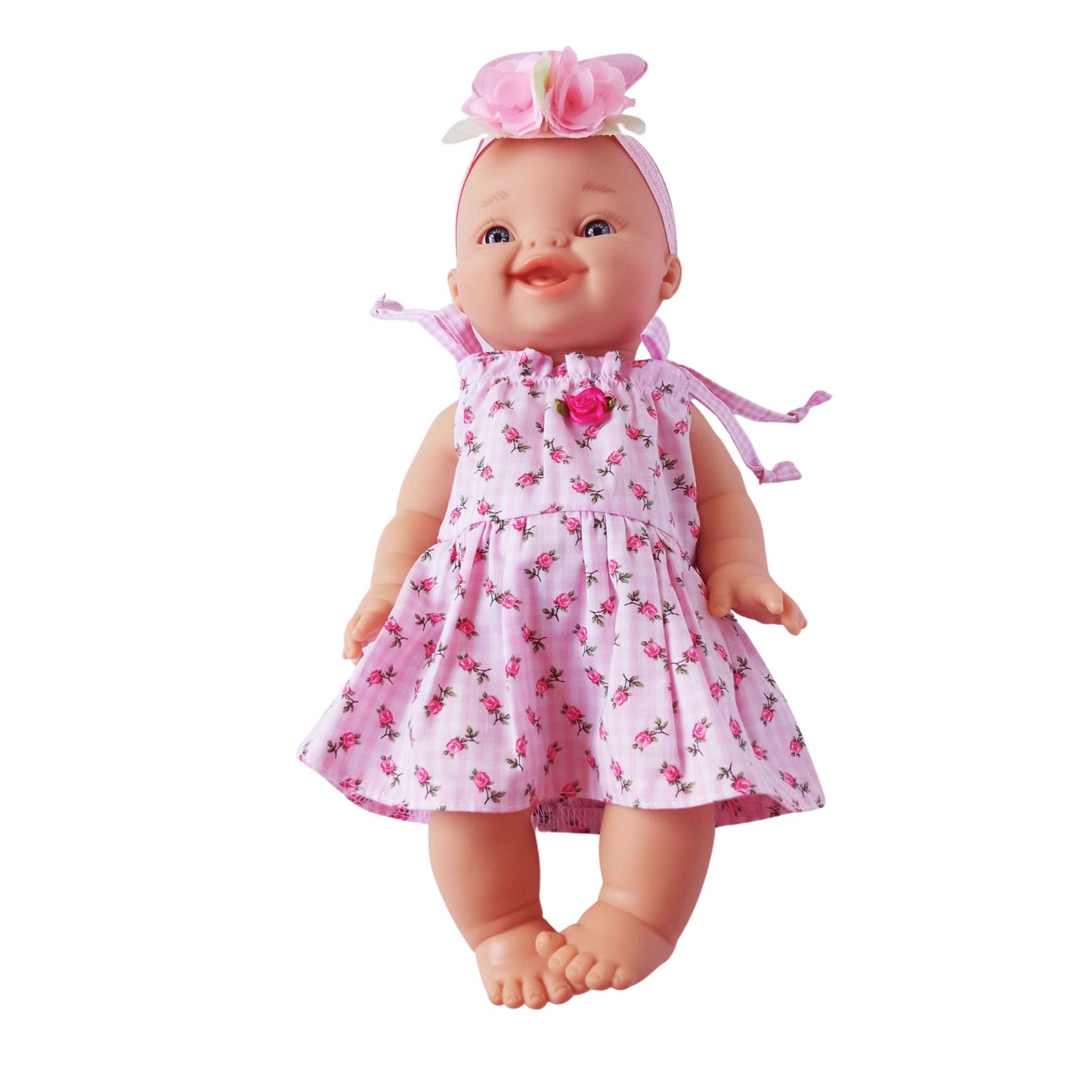 Smiling baby doll wearing a pink floral cotton summer dress with shoulder ties and rosebud decoration, made for 34 cm dolls like Paola Reina or Baby Born.