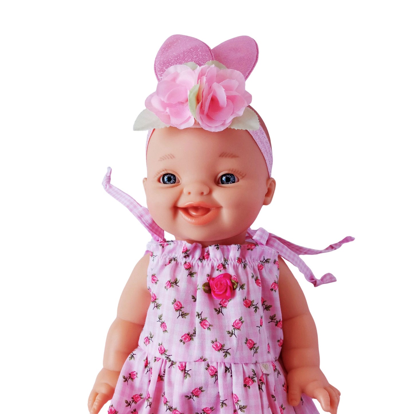 Smiling baby doll wearing a pink floral cotton summer dress with shoulder ties and rosebud decoration, made for 34 cm dolls like Paola Reina or Baby Born.