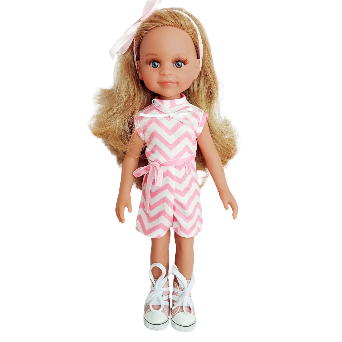 Paola Reina 32 cm doll wearing a pink and white zigzag summer jumpsuit with a ribbon belt and matching headband.