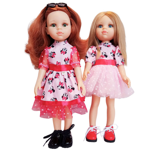 Two Paola Reina 32 cm dolls wearing matching Minnie Mouse-inspired dresses with red satin bows and polka-dot mesh details. One doll has black shoes, while the other wears red shoes.