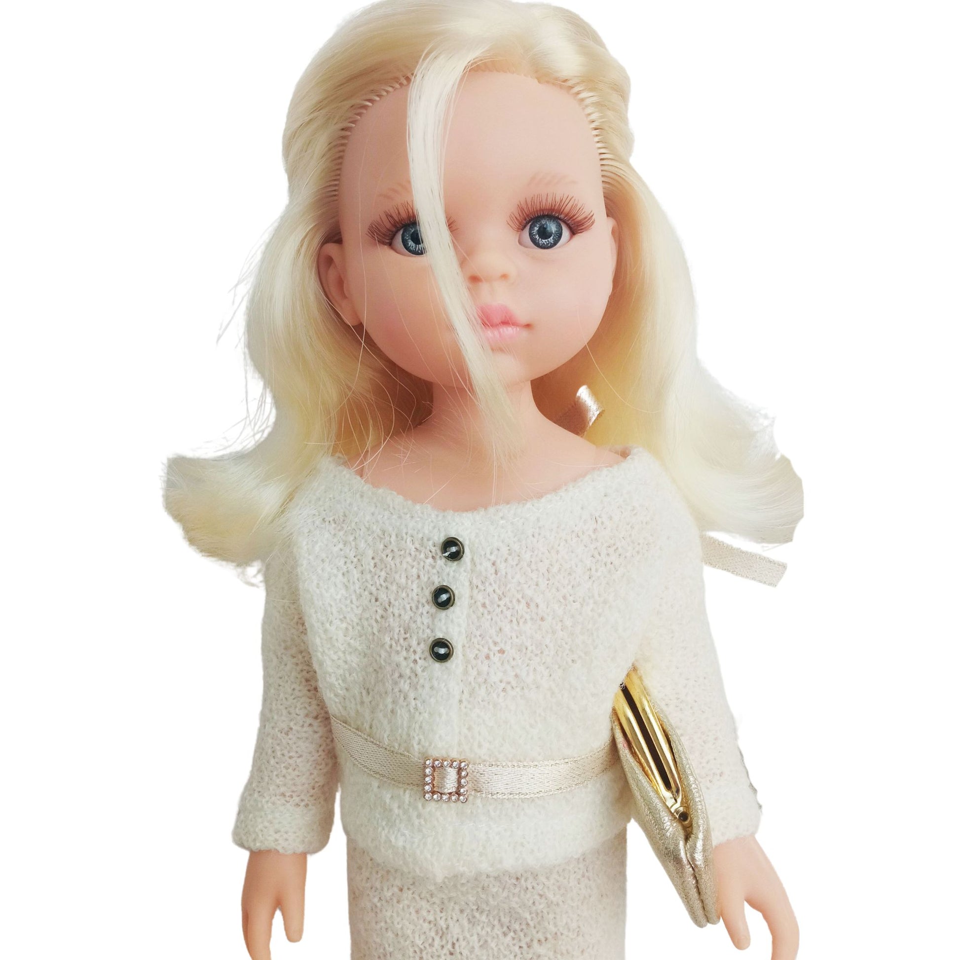 Paola Reina Las Amigas 32 cm doll dressed in a handmade knitted jersey outfit with a buttoned top, matching skirt, and a stylish belt, holding a gold clutch.