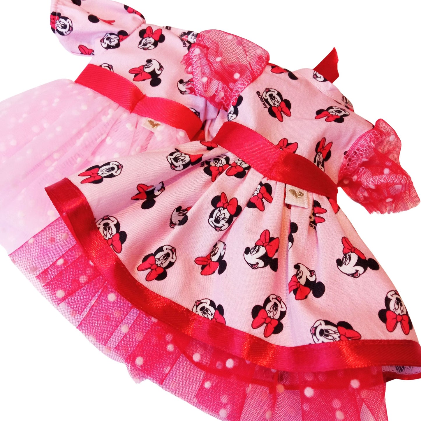 Two dress for Paola Reina 32 cm doll wearing matching Minnie Mouse-inspired dresses with red satin bows and polka-dot mesh details. 